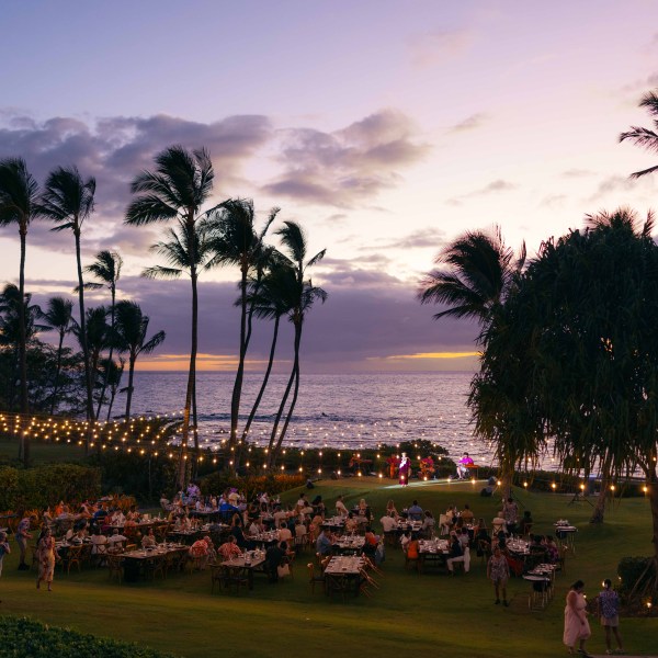 Outdoor dinner event at sunset with palm trees and ocean view.