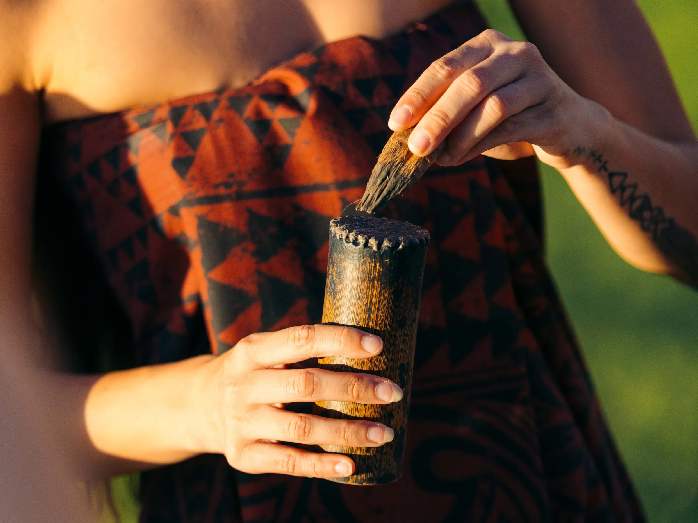 Person in patterned fabric holding a wooden cup outdoors.