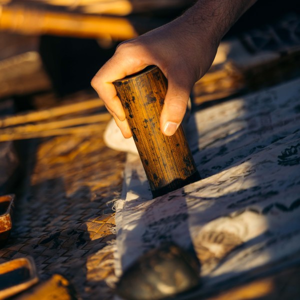 Hand holding a wooden cylinder over cloth with sunlight.