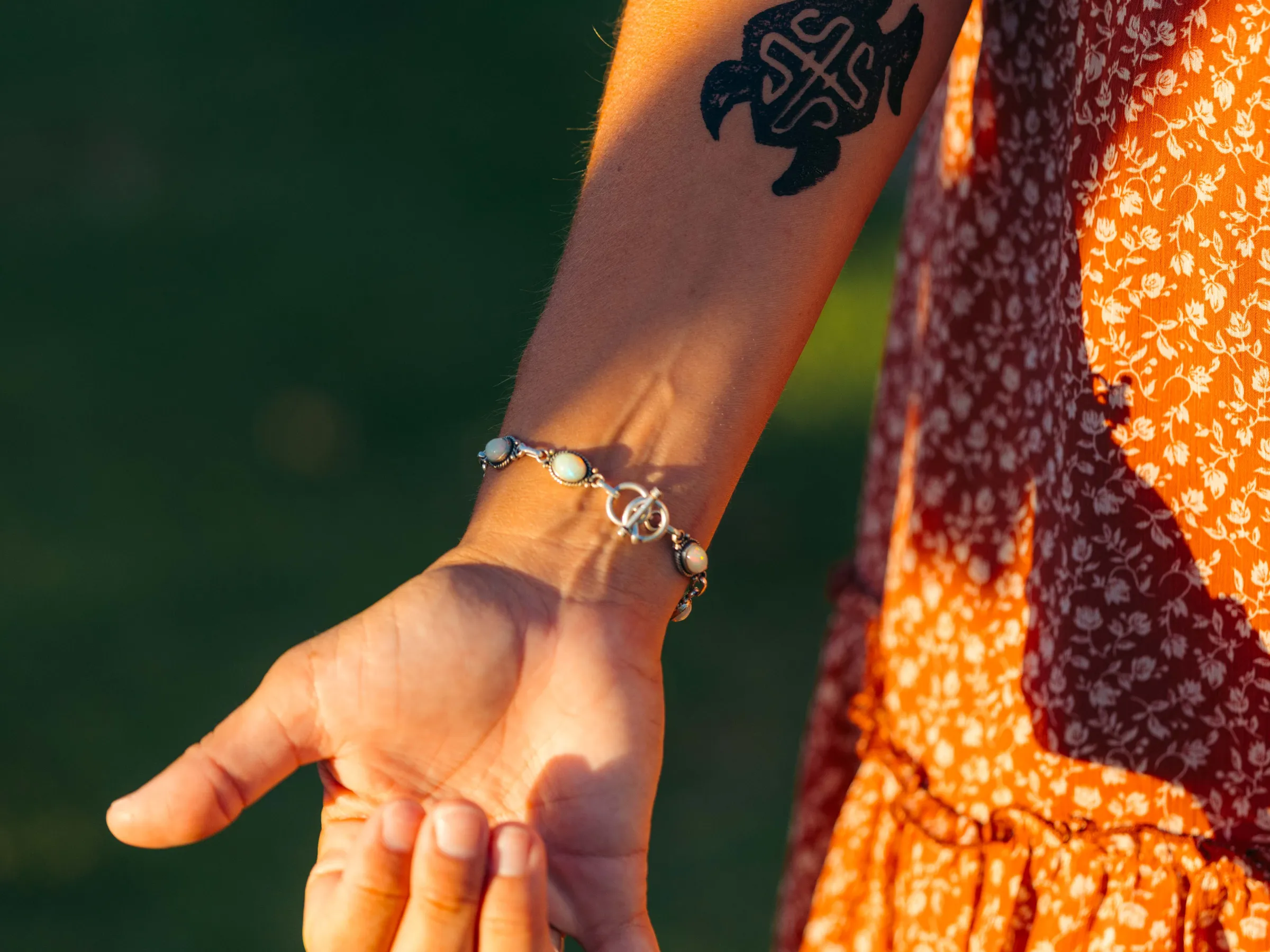 Close-up of a forearm with turtle tattoo, wearing a bracelet, in a patterned orange dress.