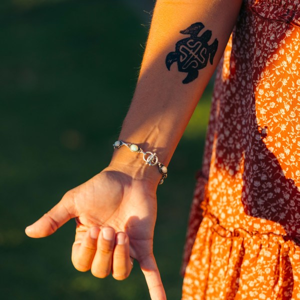 Close-up of a forearm with turtle tattoo, wearing a bracelet, in a patterned orange dress.