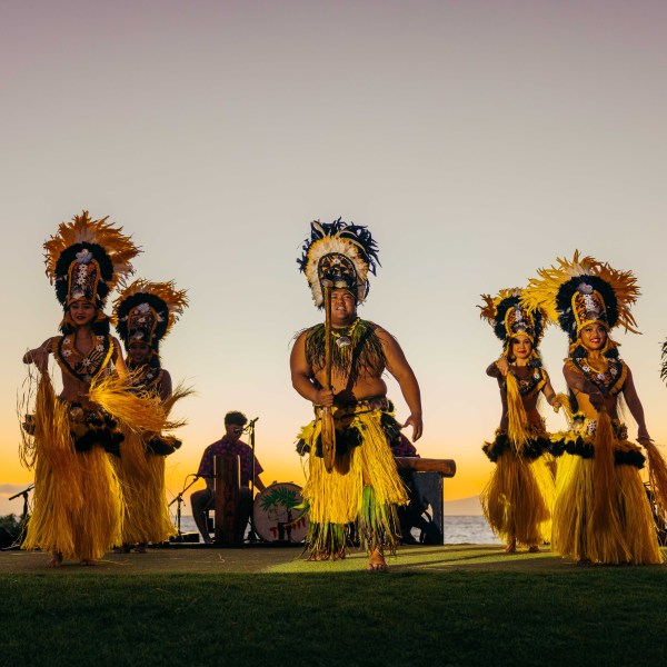 Dancers in vibrant costumes performing at sunset on a stage by the ocean.