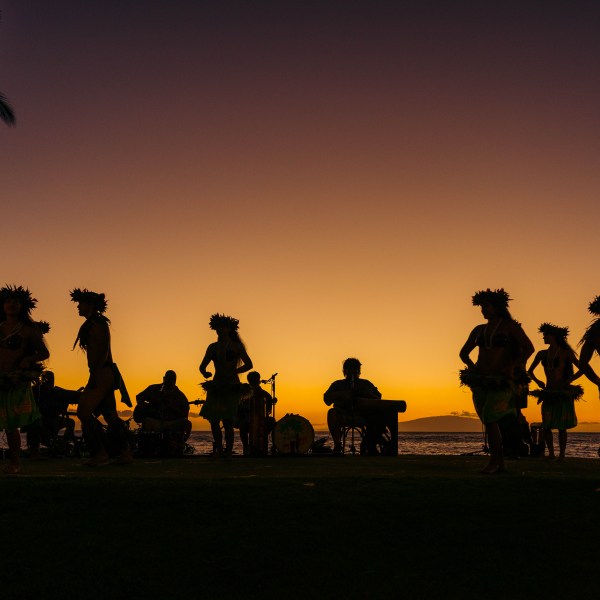 Silhouettes of dancers and musicians at sunset by the ocean.