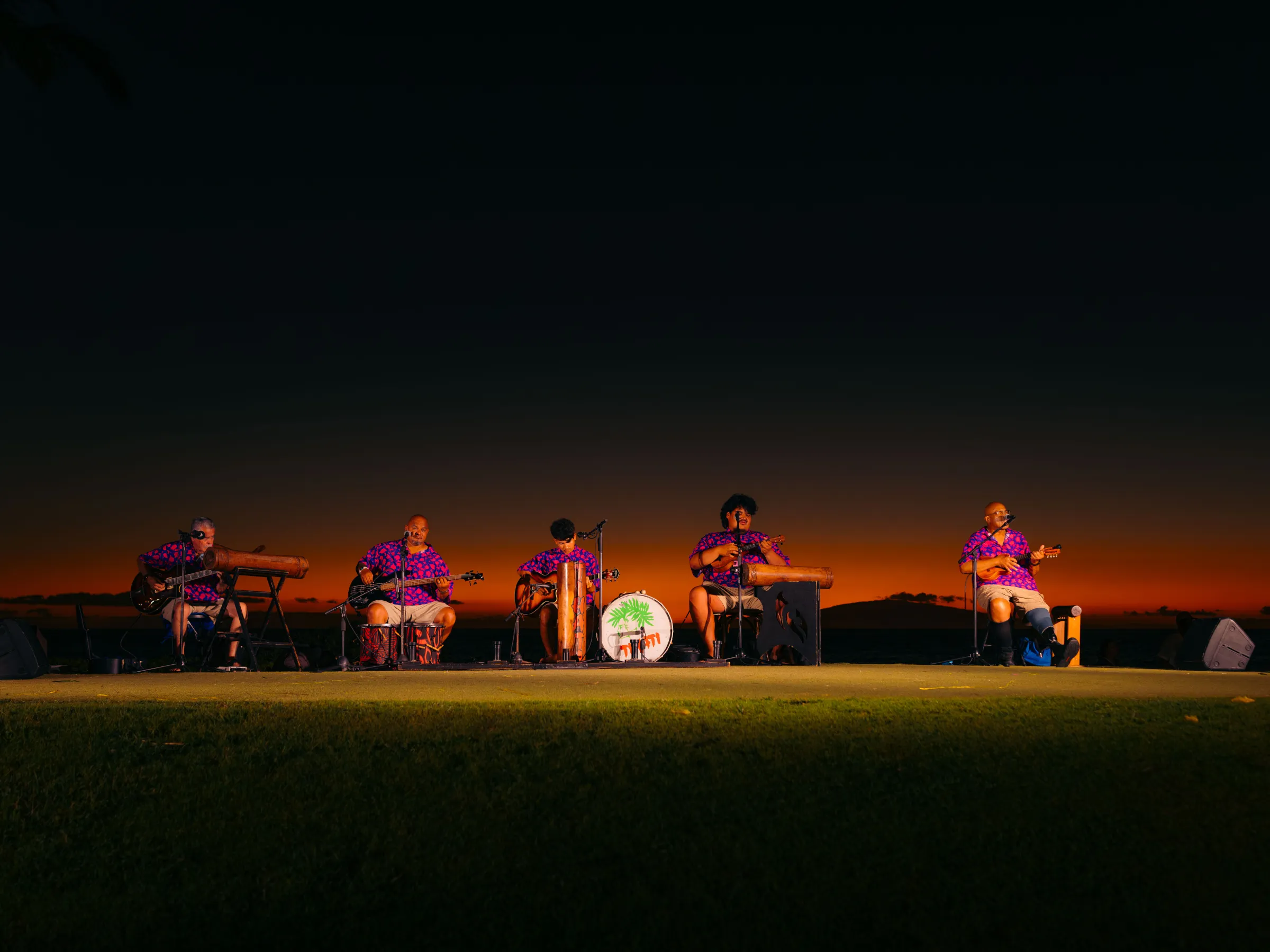 Band performs on stage at sunset, wearing matching outfits, with musical instruments.