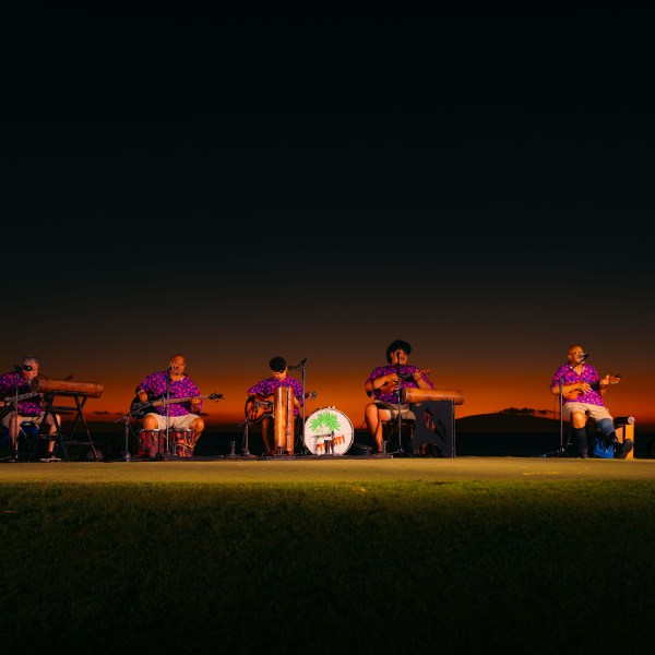 Band performs on stage at sunset, wearing matching outfits, with musical instruments.