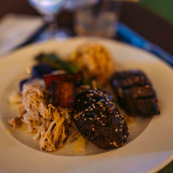 Plate with assorted meats and sides on a dark table.