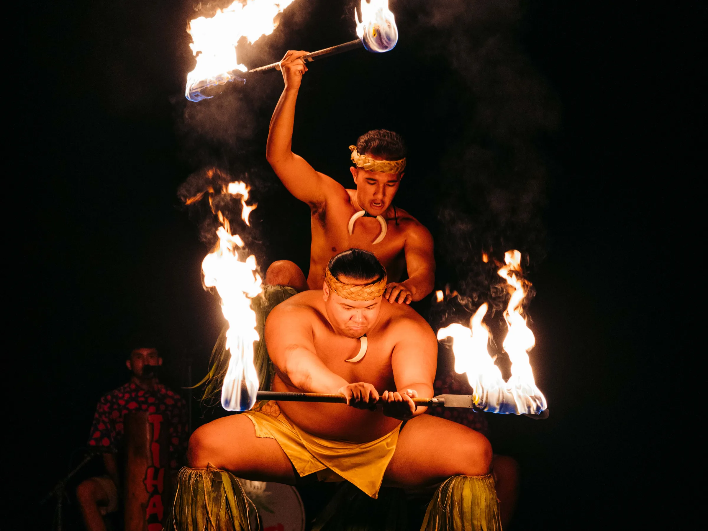 Two performers in traditional attire skillfully juggle flaming batons at night.