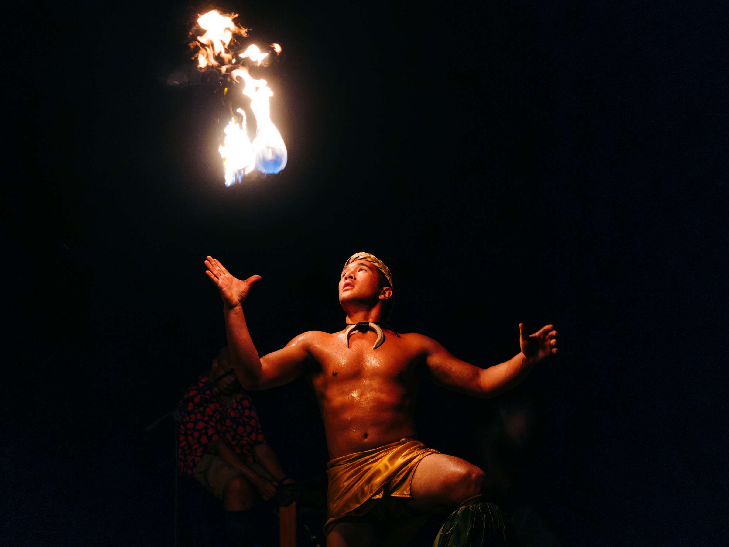 Performer kneeling and juggling fire at night.