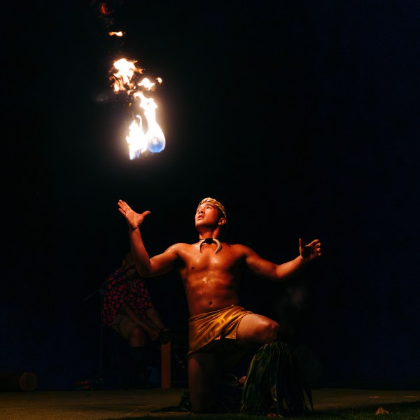 Performer kneeling and juggling fire at night.