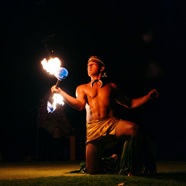 Person performing fire dance at night, kneeling with lit torches.