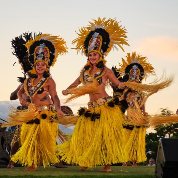 Dancers perform in traditional yellow costumes with feathered headdresses outdoors at sunset.