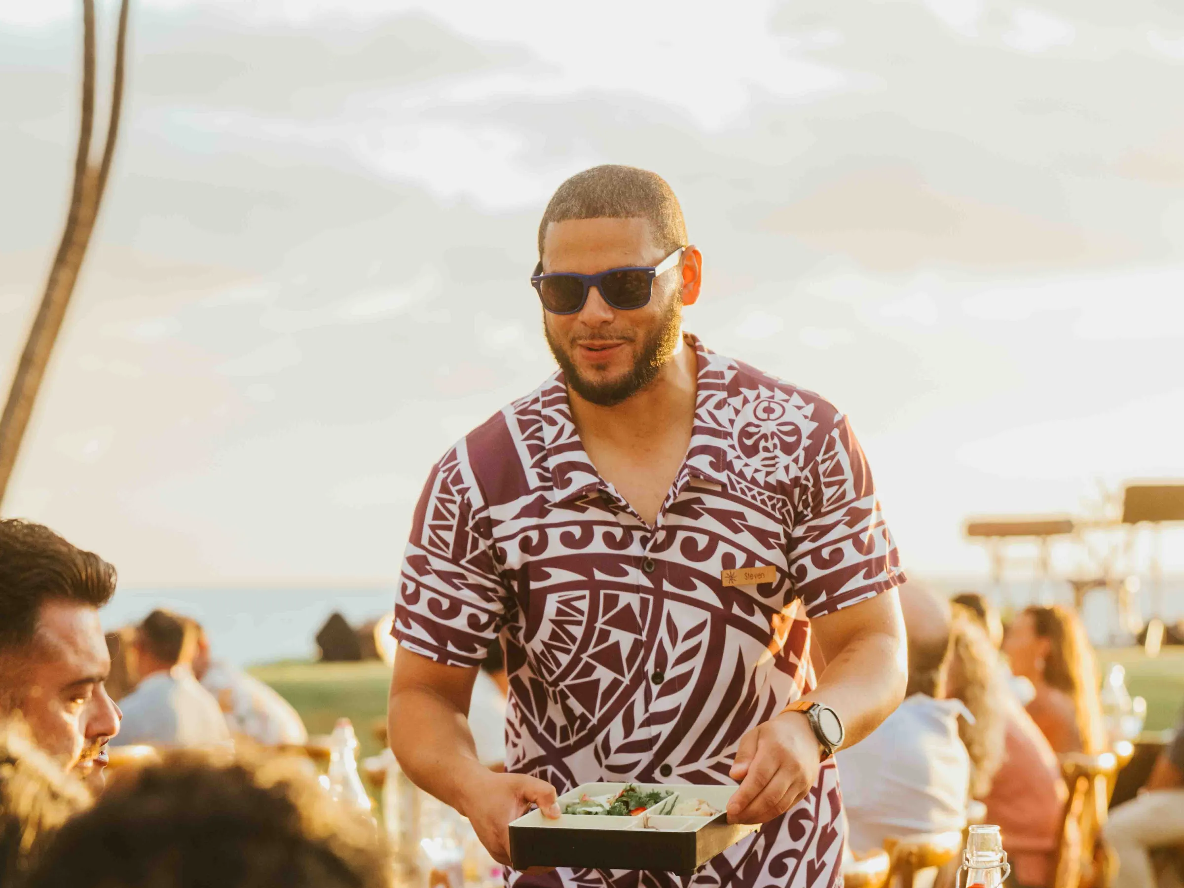 Man in sunglasses serving food at an outdoor gathering.