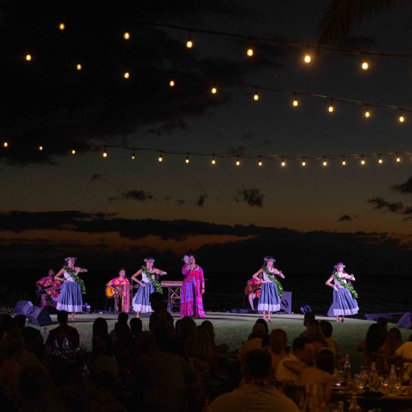 Dancers perform at night under string lights with an audience watching.