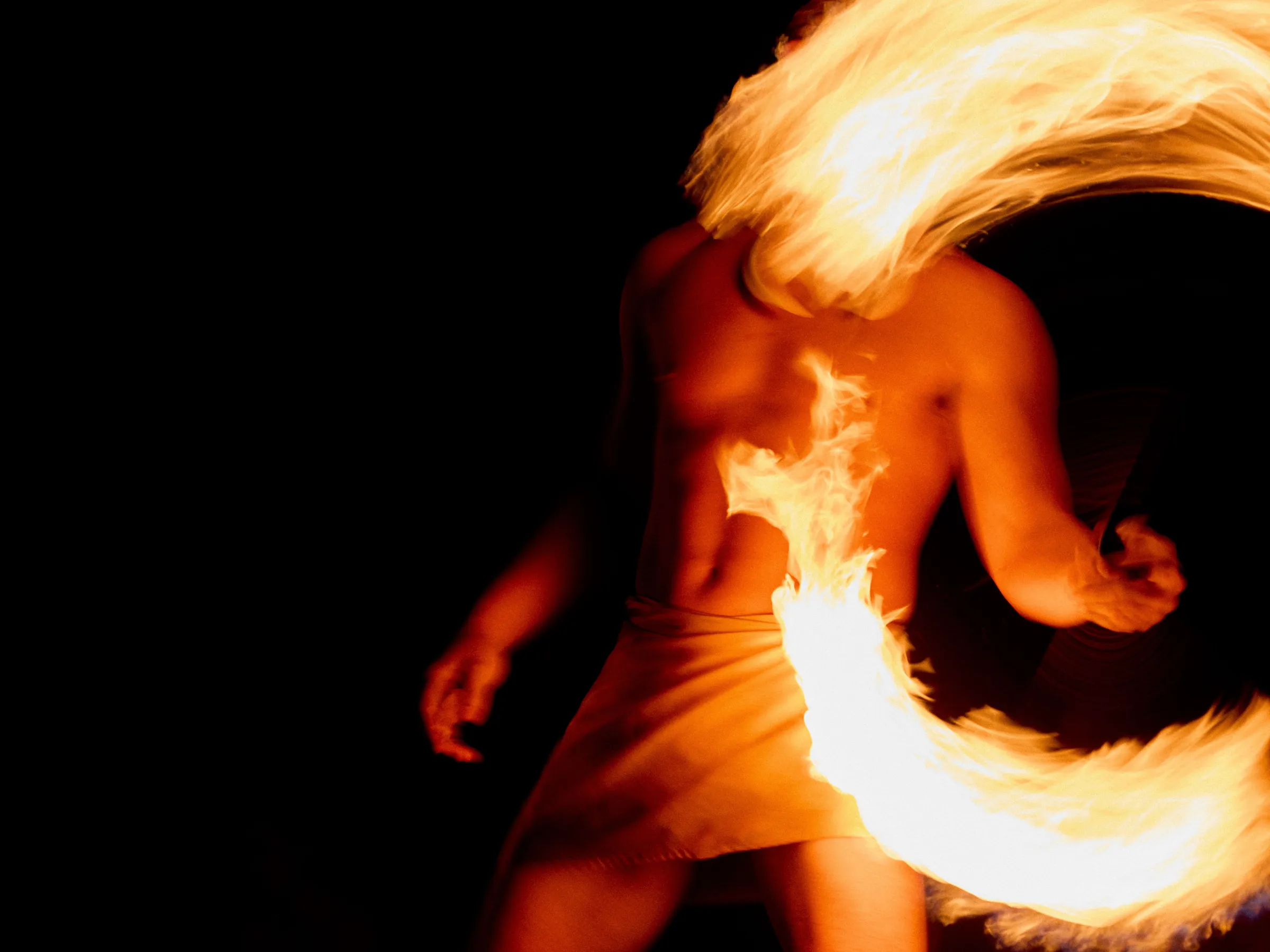 Person spinning fire, creating a fiery arc against a dark background.
