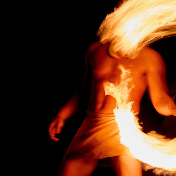 Person spinning fire, creating a fiery arc against a dark background.