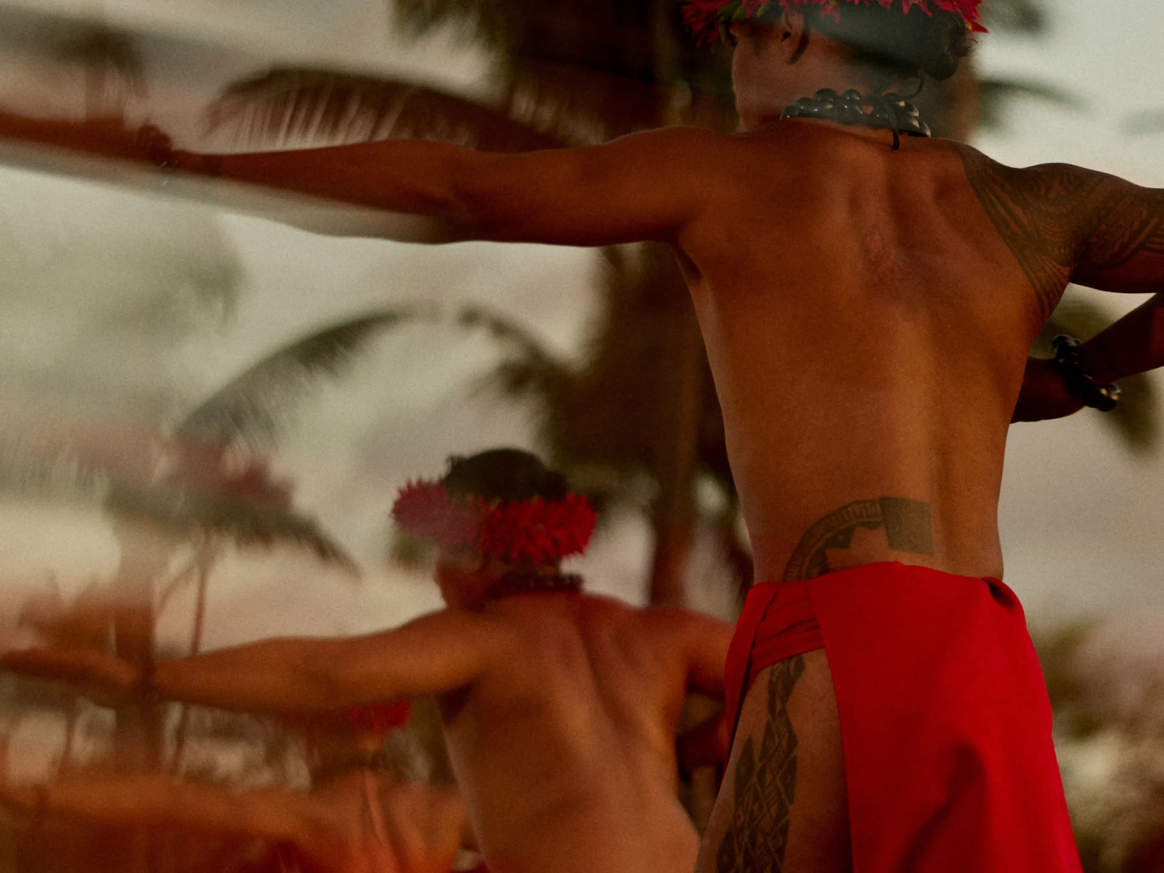 Traditional dancers in red skirts with palm trees in the background.