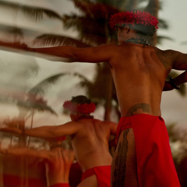 Traditional dancers in red skirts with palm trees in the background.