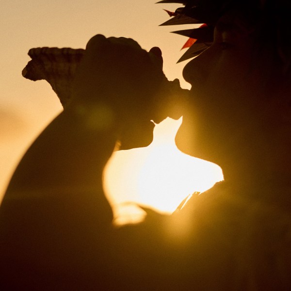Silhouette of person blowing a conch shell at sunset.
