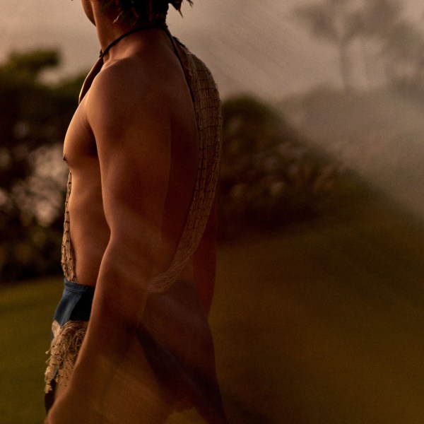 Person in traditional attire with headdress stands outdoors, sunset light.