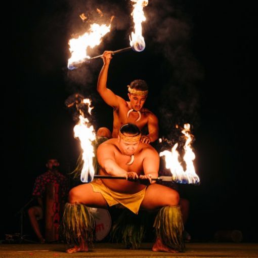 Two performers in traditional attire skillfully juggle flaming batons at night.